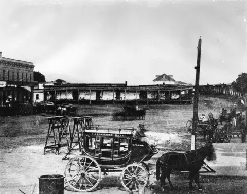 Lafayette Hotel stagecoach near the adobes in Calle de los Negros circa 1870, presently Alameda Street near Union Station and Terminal Annex Building. The old Antonio Coronel adobe is in the background.
