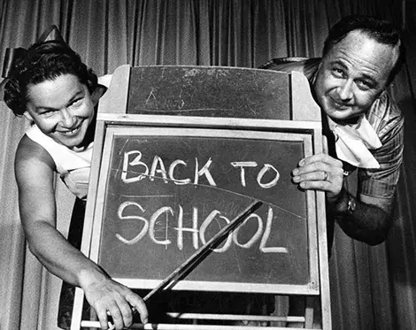 a man and a women point at a back to school sign on a chalk board