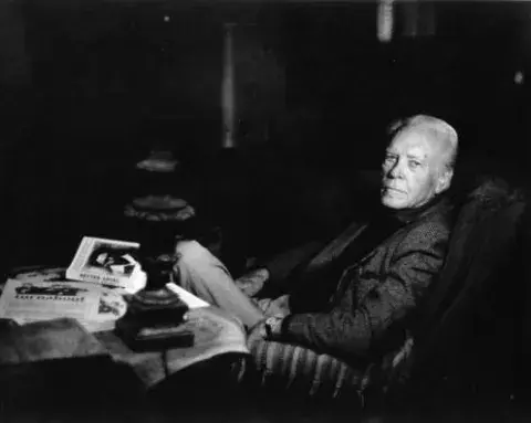 Forman Brown seated on a chair, with his book Better Angel on a table