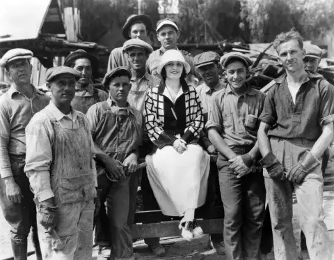 Poli Negri sitting in the middle of a group of construction workers