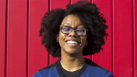 poet Dinika Kelly in front of a red wall