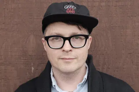 Matthew Dickman in a ball cap and glasses