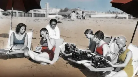 1934 colorized picture of people at the beach with typewriters