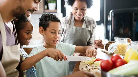 Young boy cutting vegetables with the family watching