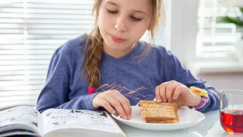 Girl reads a graphic novel while having a grilled ham and cheese sandwich