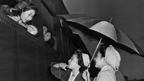 Young Japanese girls brave the early morning rain to bid farewell to friends leaving for Manzanar relocation camp