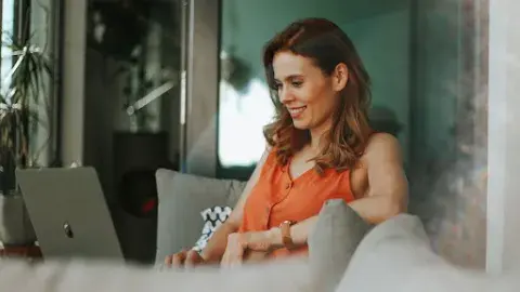 woman in an orange tank top looking at her laptop on the couch