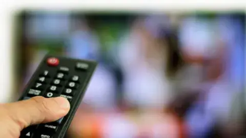hand holding a remote with a tv screen in the background