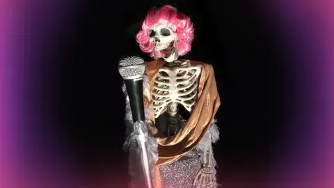 skeleton in a pink wig singing into a microphone