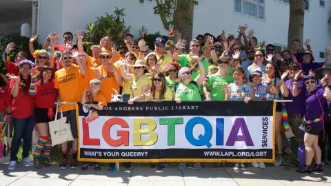 Librarians wearing rainbow colored tshirts in front of a LGBTQIA banner