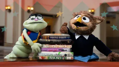 2 library puppets in the rotunda with a stack of books between them