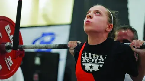 Young girl squatting a heavy barbell at a competition