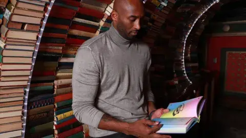 Kobe Bryant reads a book with The Last Bookstore's book tunnel in the background