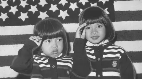 Two little girls, Pham Doan Phuong, 6, and Pham Quynh Phuong, 4, salute the American flag