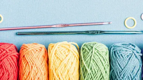 Six balls of yarn of various colors with two crochet needles on a blue background