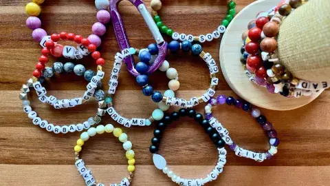Multicolored, beaded friendship bracelets are arrayed on a wooden table.