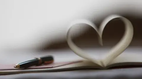 A black pen rests on an open book with pages folded to resemble a heart shape