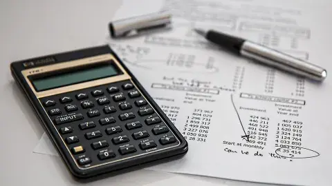 calculator on the bottom left, page with a lot of numbers and a pen on the table