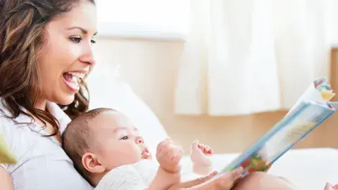 A woman holds a baby and a book