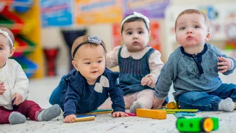 Four babies sitting up on the floor with toys in front of them