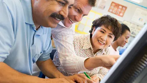 a man helps another man on a computer while a woman looks on