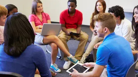 A group of teens sit in a circle for a Teen Council meeting.