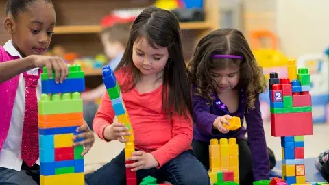 Three girls build with Lego building blocks.