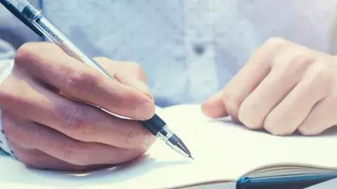 Two hands, one writing in a notebook.