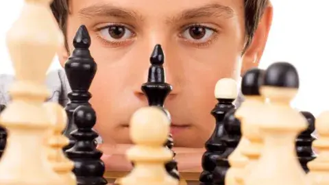 Young boy looking at chess pieces.