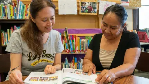 Literacy tutor and learner sitting at a table reading a book together
