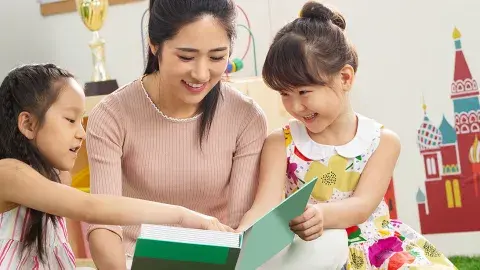 Young female teacher, volunteer reads to a group of smiling young kids.