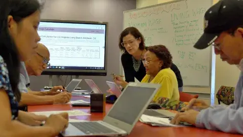 A group of adult learners sitting on a table learning computer skills