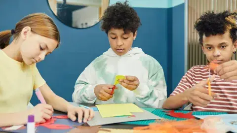 Three children cutting pieces of colorful construction paper. 