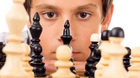 a young male peers across a black and white chess board