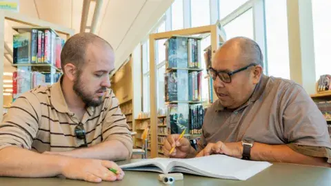 Two men sitting at a table looking at a book.