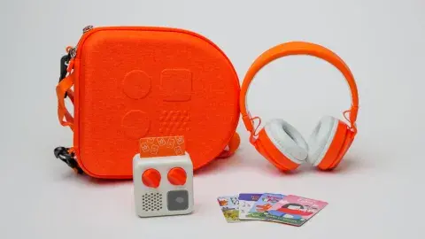 A yoto audio player displayed on a white background with an orange case, orange headphones, and four cards fanned out on the surface.