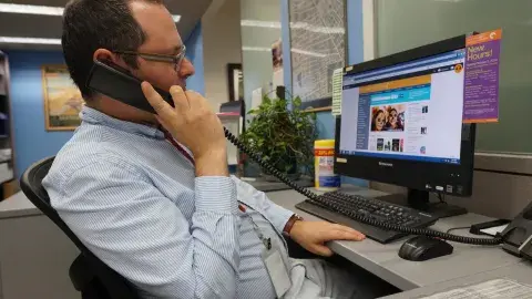 A librarian answers the phone while looking at the lapl.org website on a desktop computer.