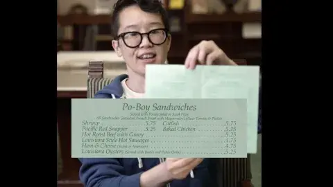 excerpt from menu that reads "po-boy sandwiches" is centered in front of person displaying menu