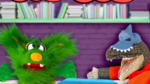 The image shows two puppets in the library. The first puppet is Ellie, a green fluffy puppet, who is confronting the Library Bandit, a masked dinosaur puppet, for stealing her books.