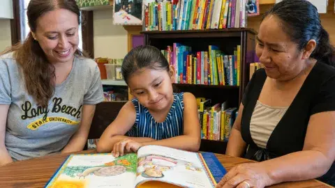 A literacy instructor, a young girl and a woman sit at a table and read a picture book.