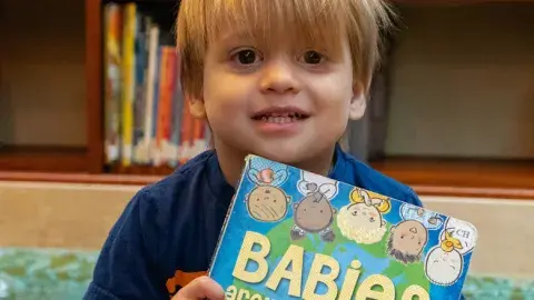Toddler holding a book entitled Babies.