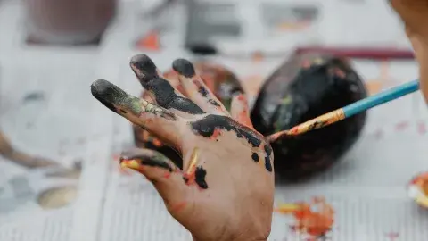A child painting their own hand with a paintbrush.
