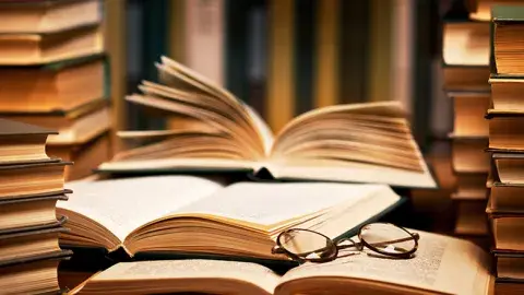 Stacks of closed and open books with a pair of glasses resting on top.