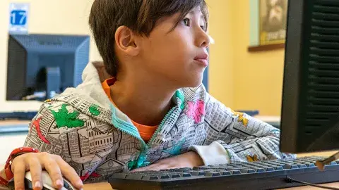 Boy sitting at computer looking at computer screen with hand on mouse