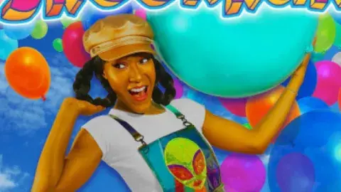 A smiling woman wearing a cap holds up a blue beach ball against a backdrop of balloons