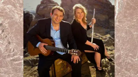 Flutist and guitarist sitting in front of a rocky landscape.