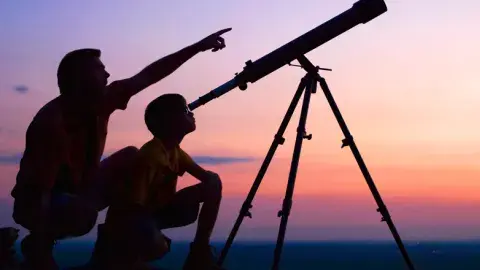 Adult and youth looking through a telescope at the night sky
