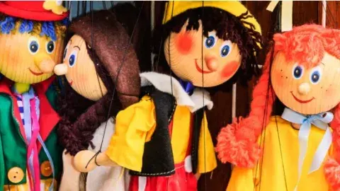 Four assorted marionettes, side-by-side, with yellow and green tops.