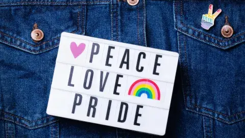 A jean jacket with a peace pride button on its pocket and a sign that says "peace, love, pride."