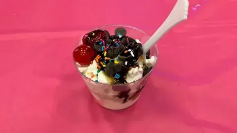 An ice cream sundae topped with cherries, sprinkles, and chocolate chips, on a pink tablecloth